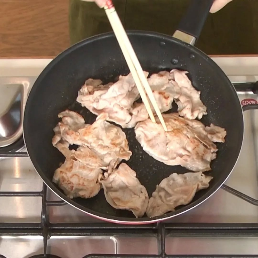 豬肉片放入煎鍋中，加入芝麻油翻炒，然後用鹽和胡椒粉調味